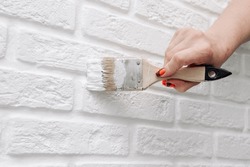 A woman paints a brick wall with white paint. She holds a brush in her hand. Bottom view