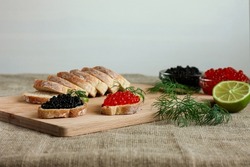 Sandwiches with red and black caviar on a wooden board. Bread with caviar and lime in the background. Red and black caviar