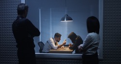 Medium shot of a male and a female investigator watching their colleague interrogating a drug dealer