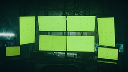 Modern computers with green screens placed on desk in dark room with shimmering lamps on illegal hacker base at night
