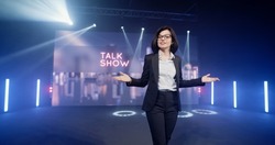 Happy presenter in a suit and glasses running onto the stage and announcing the start of the famous comedy, late-night show in an illuminated room with LED screen and 3D inscription