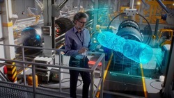 An engineer uses a tablet with a holographic innovative application, to model and design and monitor a 3D model of an aircraft engine while on an automated robotic line at an aerospace factory