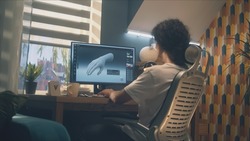 Male designer sitting on chair at the table at home office and making 3D prototype of human hand in professional program for 3D, modelling using pc.
