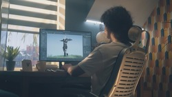 Male 3D designer sitting at the table at home and making animation for video game character, using modern computer and software for creating 3D modeling projects