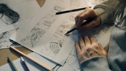 Young female artist draws sketches of comic book characters on a sheet of paper. The illustrator creates a storyboard. Storytelling concept. Video editing.