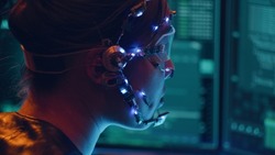 Side view of an Asian girl with futuristic headset and microphone programming using multiple computer screen. Cyperpunk style. Sci-fi background.