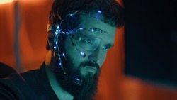 Brunette guy works on the computer with neon lights in background. Cyberpunk. Wearing a futuristic one-eyed glasses and microphone. Cyber and sci-fi backgrounds.