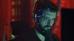 A Cyberpunk guy looks at the computer screen. Wearing futuristic one-eyed glasses with earpiece and microphone. Cyber and sci-fi backgrounds.