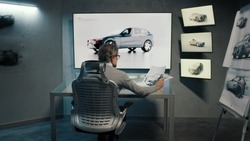 Back view of an automotive graphic designer draws sketch of the prototype model of a car using stylus pen in a high tech innovative laboratory. Automotive industry. Modern studio with LED.