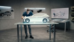 An automotive engineer and designer works on a prototype model car in a modern studio with bright LED of an automotive company. Making Design Corrections.