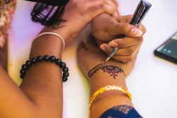 A female applying mehndi tattoo over the woman's hand