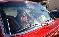 Skeleton driving a car, waving his hand out of a window. This is a Halloween or dia de los muertos themed car that is red and chrome