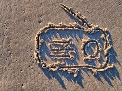 Radio receiver symbol drawn in sand of a sea beach during sunset.