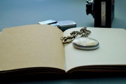 old vintage pocket watch placed on notebook, lighter, old photo film camera, concept of vintage travel accessories