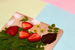 wooden plank with strawberry slices, leaves, flowers and petals idyllic scene from paradise