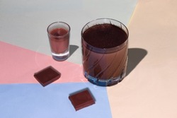 small and a large cup of chocolate and two cubes of chocolate on a colorful pastel background