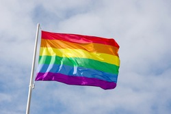 Rainbow flag, a symbol for the LGBT community, waving in the wind with a cloudy background