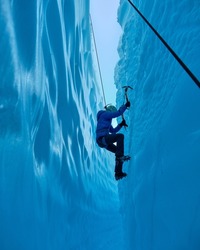 Adventurous Girl Ice Climbing in Slot Canyon on Blue Matanuska Glacier in Alaska. Glacier is receding and melting due to global warming. Ice climbing equipment is visible.