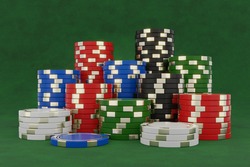 Stacked poker chips isolated on green background. Black, blue, red, green and white casino chips with golden elements on green table. 3d render.