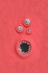 Monster with three ugly eyes and a mouth with sharp teeth, fabulous creature made by hand from pink plasticine. Comic facial expressions. Ugly and crazy face of alien monster
