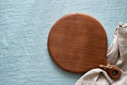 Food background mockup with round wooden cutting board on blue linen textile tablecloth backdrop. Top view, copy space. Menu, recipe, mock up for baking dessert and cupcakes