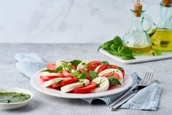 Horizontal of italian caprese salad with pesto sauce. Fresh mozarella, sliced tomatoes, basil leaves, olive oil. Arranged vegetarian mediterranean food. Healthy starter. Dietary antipasto
