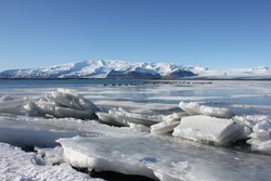 Big ice blocks on the shore of the Jökulsárlón glacier lagoon with Vatnajökull glacier in the background reflecting itself in the cold blue water during a sunny winter day in the south of Iceland