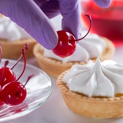 A woman pastry chef decorates a cake with a cocktail cherry. Production of pastries and cakes.