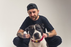 Adorable bond between pedigree dog and its owner. European bearded tattooed man in black clothes sitting in a studio with his pedigree dog. Blurred dog in the foreground. Looking at camera together