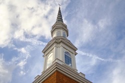 Tower spire of church pointing upwards into a cloudy blue sky