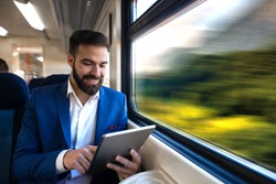 Businessman sitting next to window reading news and surfing internet on his tablet while traveling in comfortable high speed train.