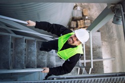 Top view of factory worker climbing metal stairs on industrial silo building.