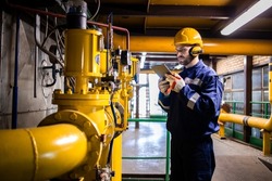 Industrial worker checking gas pipe pressure and consumption in refinery plant.