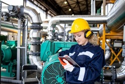 Female factory worker working on tablet computer in oil and gas refinery plant.