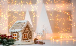 Christmas decorations with light behind it, creating a nice blurry boken. Christmas or new year still life with ornaments on rustic white table. Homemade gingerbread house. Copy space for text.