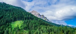 Landscape of the Alps. Mountain peaks and beautiful forest. Freedom, tourism, travel. Peaks on a background of white clouds and blue sky. Green hills and dense forests on the slopes.