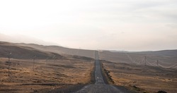 Vintage photo of a country road. Empty road through the desolate hilly area. Cloudy sky and horizon in a haze. Concept landscape. Rural scene.