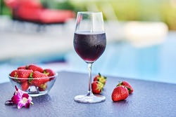 Red wine glass with strawberries on a table on the beach.