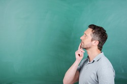 Thoughtful mature male teacher with hand on chin against blank blackboard