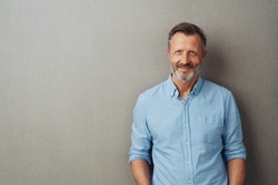 Relaxed attractive smiling middle-aged man with rolled up sleeves posing against a grey studio background with copy space