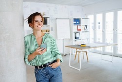 Happy young woman with a beaming vivacious smile leaning against an internal pillar in a spacious high key office looking to the side with copyspace