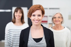 Pretty Young Office Woman Smiling at the Camera Against her Two Female Colleagues