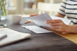 Person seated at a table with a cup of coffee reading a paper document, close up view of the hands