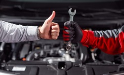 Crop unrecognizable businessman showing thumb up gesture while standing with auto mechanic with wrench in hand near broken car in garage