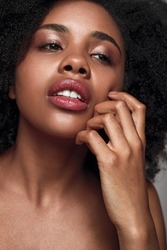 Unhappy African American female model looking away and scratching skin on cheek while being dissatisfied with appearance