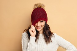 young woman wearing knitted pullover over beige background. Happy smiling girl in winter hat