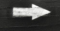 White arrow on a dark gray wall. Black concrete background with white arrow graffiti 