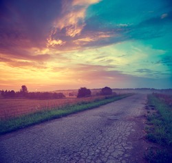 Summer Landscape with Field and Country Road Leading in the Fog. Dramatic Sky at Sunset Background. Beautiful Nature Background. Toned Photo with Copy Space.