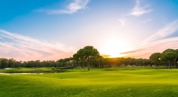 Panorama of golf course at sunset with beautiful sky. Scenic panoramic view of golf fairway. Golf field with pines