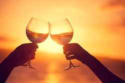 Man and woman clanging wine glasses with champagne at sunset dramatic sky background
